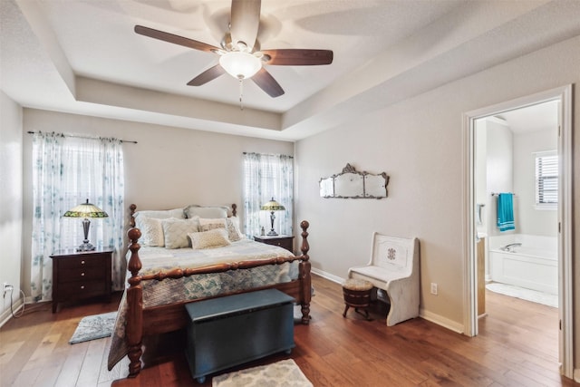 bedroom featuring a raised ceiling, hardwood / wood-style flooring, and multiple windows