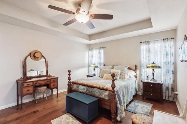 bedroom with a raised ceiling, dark wood-type flooring, and ceiling fan