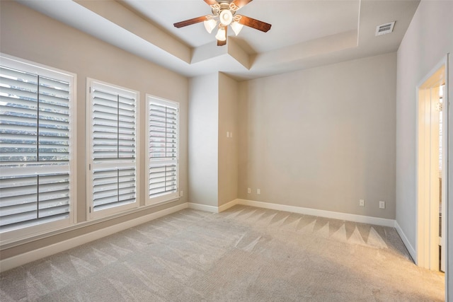 spare room with ceiling fan, a tray ceiling, and light carpet