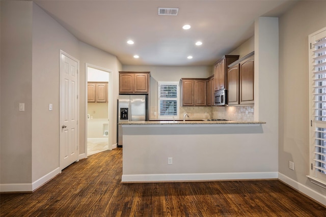 kitchen featuring dark hardwood / wood-style floors, decorative backsplash, light stone counters, kitchen peninsula, and stainless steel appliances