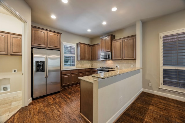 kitchen featuring tasteful backsplash, dark hardwood / wood-style flooring, kitchen peninsula, stainless steel appliances, and light stone countertops