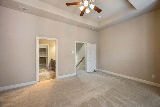 unfurnished bedroom featuring a raised ceiling, a spacious closet, light carpet, and ceiling fan