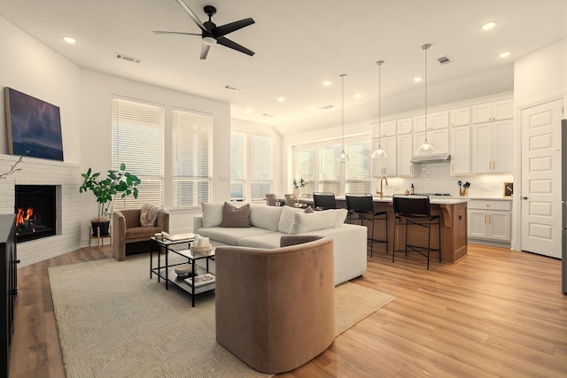 living room featuring a brick fireplace, light hardwood / wood-style flooring, sink, and ceiling fan