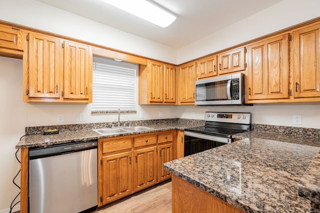 kitchen with sink, stainless steel appliances, dark stone counters, and light wood-type flooring