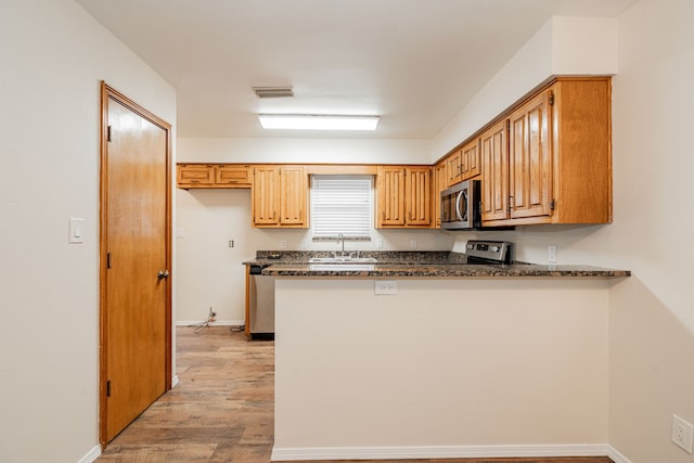 kitchen with sink, appliances with stainless steel finishes, dark stone countertops, light hardwood / wood-style floors, and kitchen peninsula