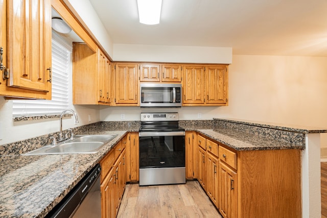 kitchen with stainless steel appliances, sink, light hardwood / wood-style flooring, and dark stone counters