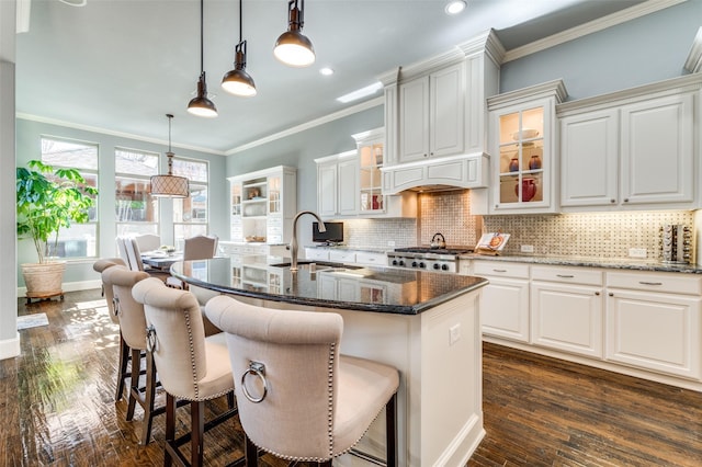 kitchen with pendant lighting, a breakfast bar area, dark stone countertops, an island with sink, and white cabinets