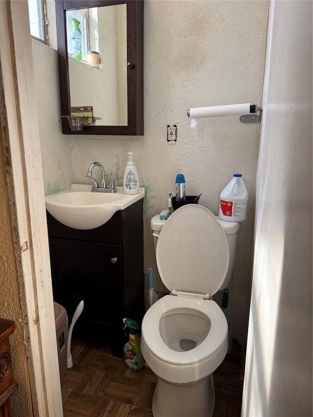 bathroom featuring parquet flooring, vanity, and toilet