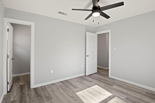 unfurnished bedroom featuring ceiling fan, a walk in closet, and light hardwood / wood-style floors