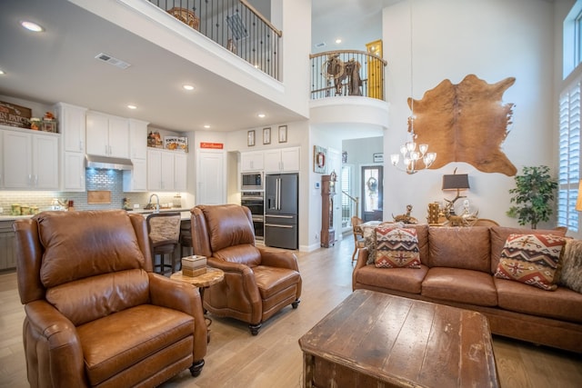 living room with a towering ceiling, a chandelier, sink, and light wood-type flooring