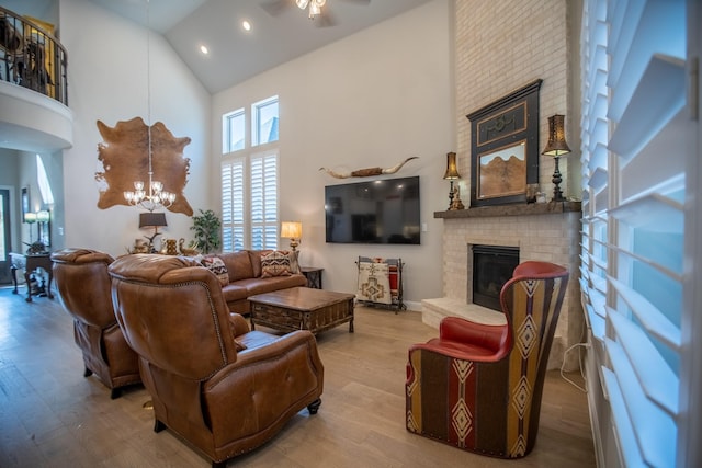 living room featuring high vaulted ceiling, light wood-type flooring, ceiling fan with notable chandelier, and a fireplace