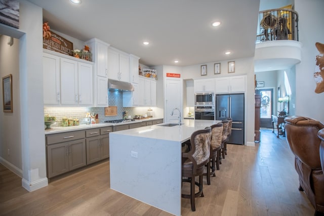 kitchen with white cabinetry, a kitchen bar, built in appliances, and a center island with sink