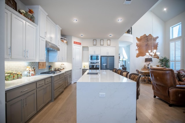 kitchen with sink, light hardwood / wood-style flooring, white cabinetry, built in appliances, and decorative backsplash