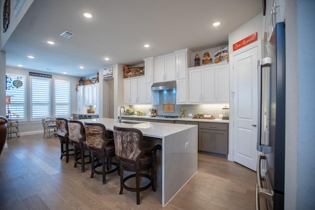 kitchen featuring sink, a center island with sink, light hardwood / wood-style floors, white cabinets, and a kitchen bar