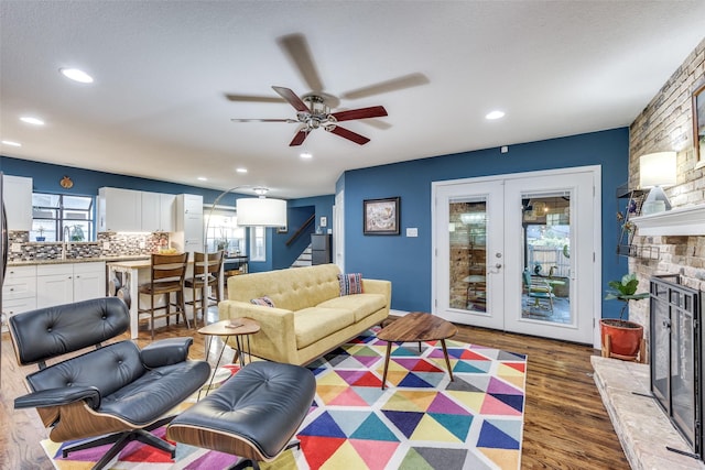 living room with a stone fireplace, sink, ceiling fan, dark wood-type flooring, and french doors