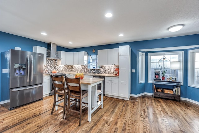 kitchen featuring wall chimney range hood, appliances with stainless steel finishes, tasteful backsplash, a healthy amount of sunlight, and white cabinets