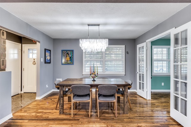 dining area with a textured ceiling, wood-type flooring, french doors, and a chandelier