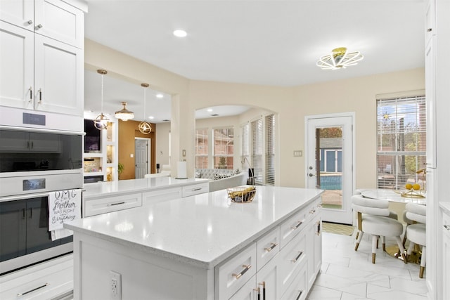 kitchen featuring a center island, white cabinets, double oven, and decorative light fixtures