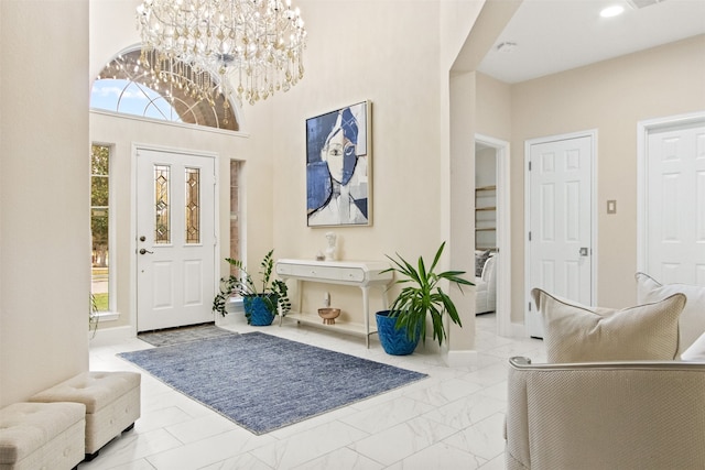 foyer entrance featuring a towering ceiling, a healthy amount of sunlight, and a chandelier