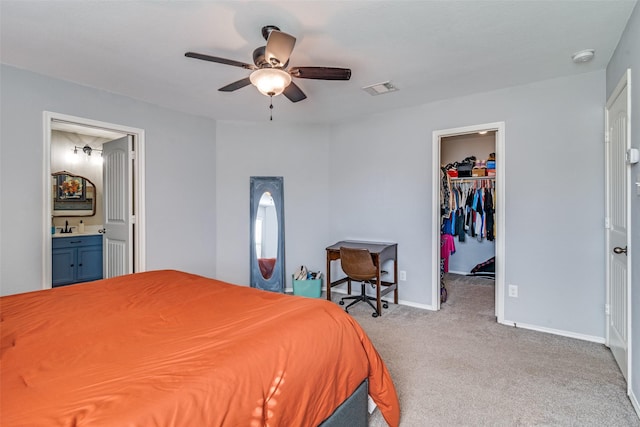 carpeted bedroom with sink, a walk in closet, ceiling fan, ensuite bath, and a closet