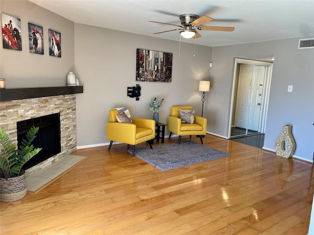 living area with ceiling fan, a fireplace, and light wood-type flooring