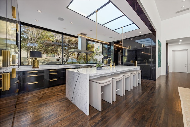 kitchen with a skylight, wall chimney exhaust hood, modern cabinets, and light stone counters