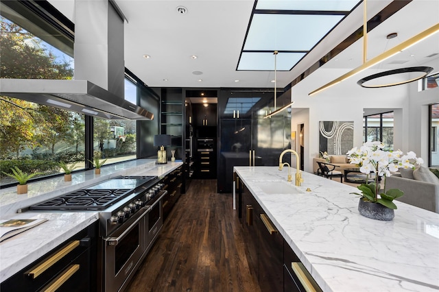 kitchen featuring a sink, open floor plan, double oven range, light stone countertops, and wall chimney exhaust hood