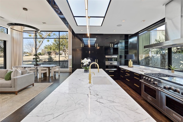 kitchen with range with two ovens, light stone counters, a healthy amount of sunlight, a sink, and modern cabinets