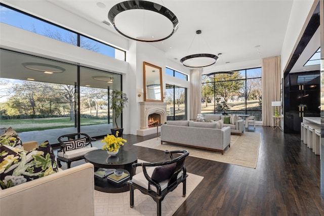 living area featuring a warm lit fireplace, a high ceiling, and wood finished floors