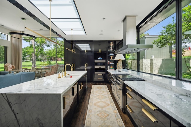 kitchen with island range hood, decorative light fixtures, a large island with sink, stainless steel appliances, and light stone countertops