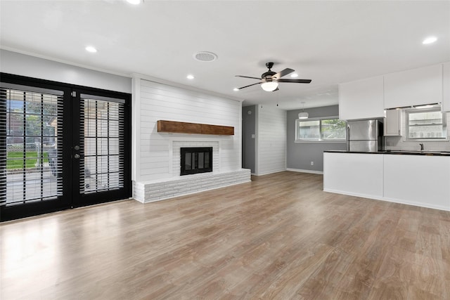 unfurnished living room featuring french doors, sink, light wood-type flooring, ceiling fan, and a fireplace