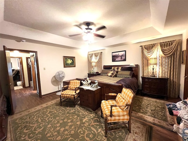 bedroom with a raised ceiling, ceiling fan, dark hardwood / wood-style floors, and a textured ceiling