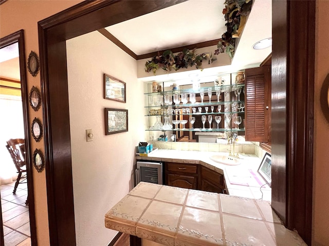 bar featuring sink, tile counters, ornamental molding, and beverage cooler