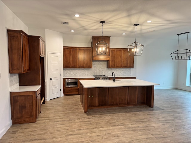 kitchen featuring pendant lighting, sink, light hardwood / wood-style flooring, and a center island with sink