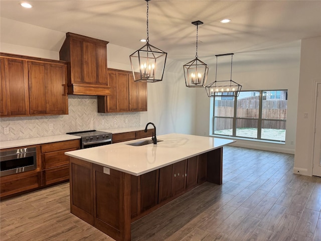 kitchen with sink, appliances with stainless steel finishes, a kitchen island with sink, decorative backsplash, and decorative light fixtures