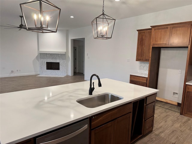 kitchen with pendant lighting, sink, dishwasher, a tiled fireplace, and light wood-type flooring