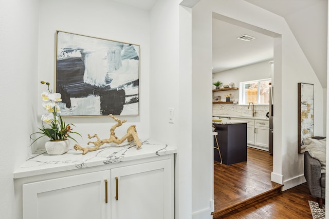 bar with sink, white cabinetry, tasteful backsplash, dark hardwood / wood-style flooring, and light stone countertops