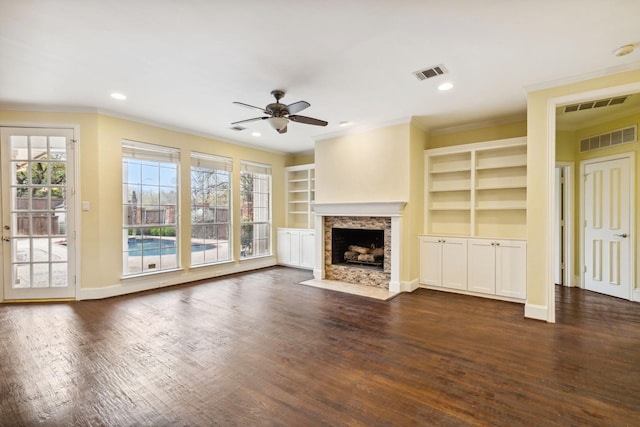 unfurnished living room featuring built in features, dark wood-type flooring, ornamental molding, and ceiling fan