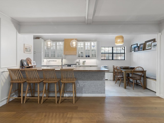 kitchen featuring decorative light fixtures, beamed ceiling, white cabinets, a kitchen breakfast bar, and light hardwood / wood-style flooring