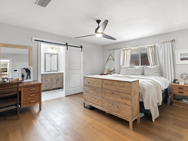 bedroom with a barn door, connected bathroom, ceiling fan, and light hardwood / wood-style flooring