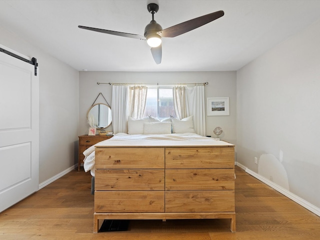 bedroom with ceiling fan, wood-type flooring, and a barn door