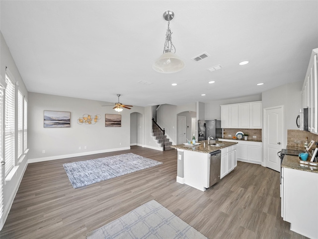 kitchen featuring white cabinetry, black refrigerator with ice dispenser, hanging light fixtures, stainless steel dishwasher, and a kitchen island with sink