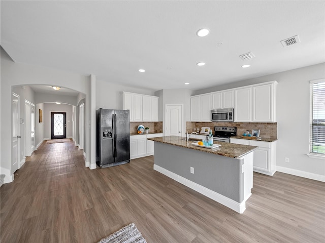 kitchen featuring white cabinetry, light hardwood / wood-style flooring, dark stone countertops, an island with sink, and stainless steel appliances