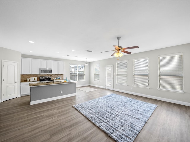 kitchen with white cabinetry, tasteful backsplash, appliances with stainless steel finishes, dark hardwood / wood-style floors, and a kitchen island with sink