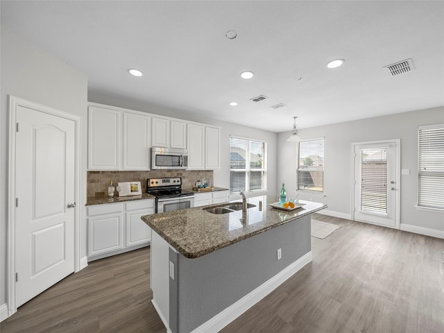 kitchen with sink, a kitchen island with sink, backsplash, stainless steel appliances, and white cabinets