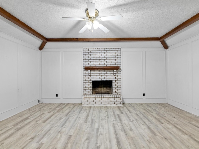 unfurnished living room featuring beamed ceiling, a textured ceiling, a brick fireplace, and light hardwood / wood-style flooring