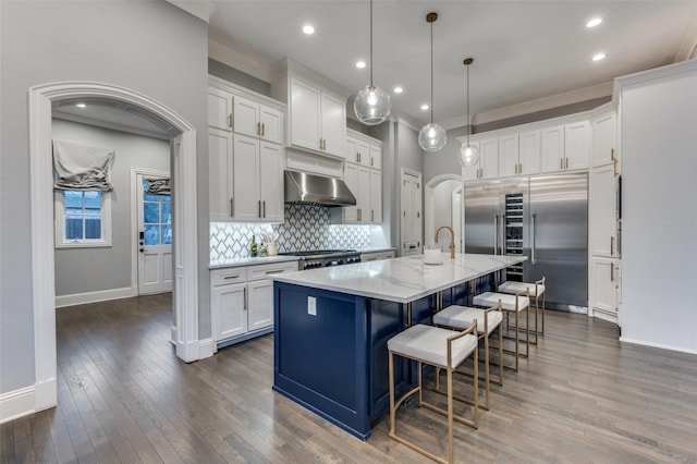 kitchen with white cabinets, decorative light fixtures, a center island with sink, and exhaust hood