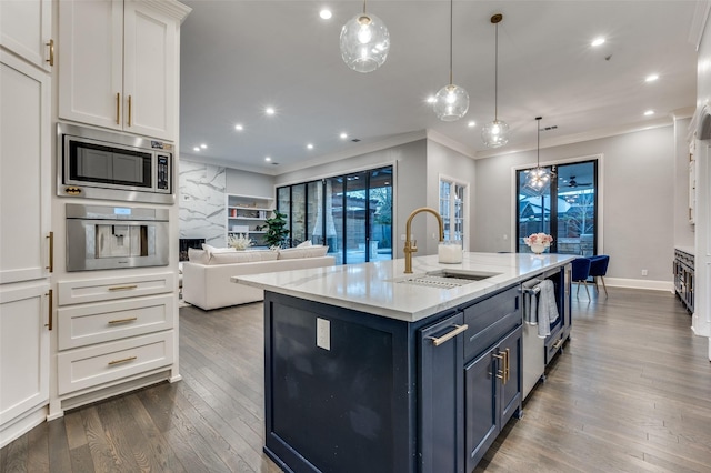 kitchen with pendant lighting, stainless steel appliances, white cabinets, and a center island with sink