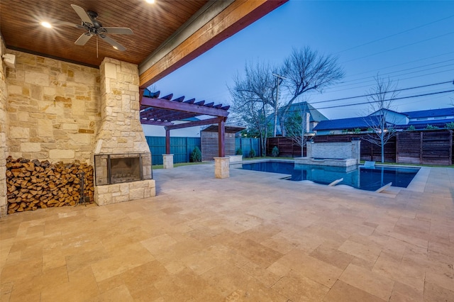 patio terrace at dusk featuring an outdoor stone fireplace, a pool with hot tub, ceiling fan, and a pergola