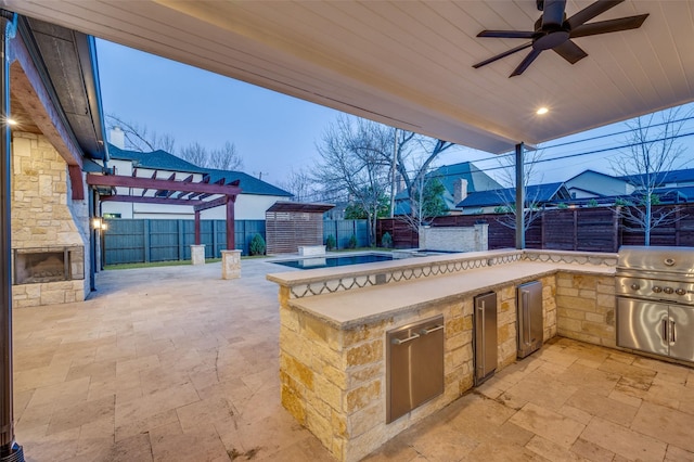 patio terrace at dusk featuring ceiling fan, grilling area, exterior kitchen, and a pergola